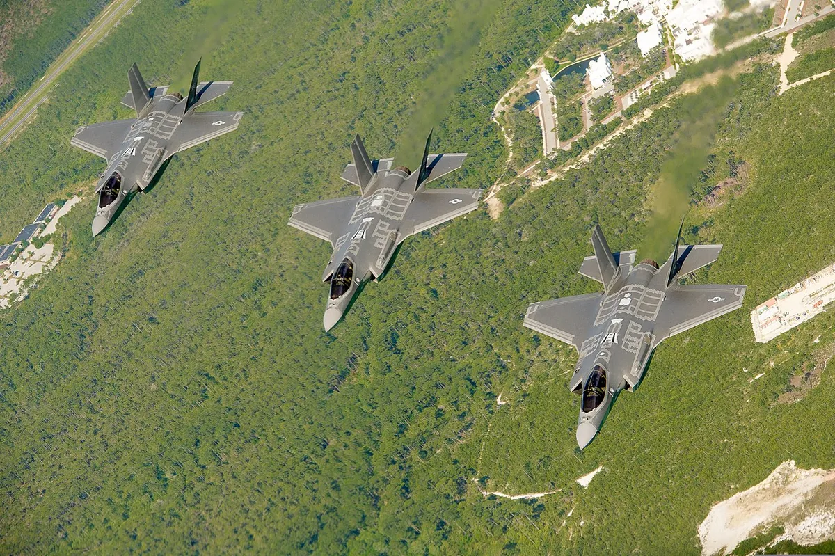 Three F-35A Lightning II jets flying in formation over the forests and white sand of the Eglin Air Force Base area