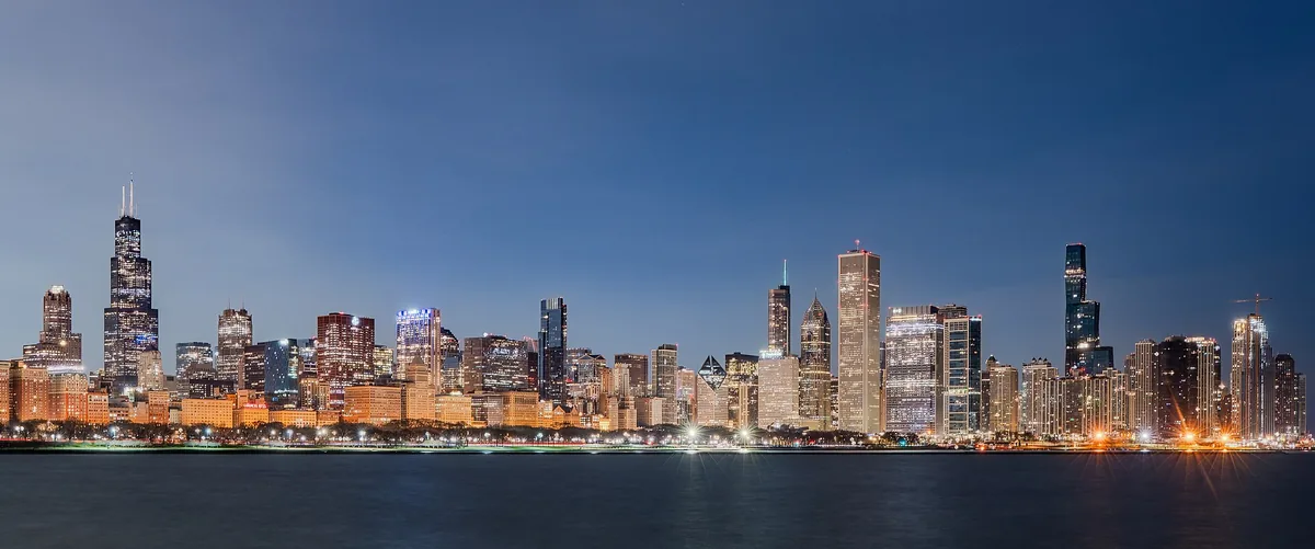 The Chicago skyline along Lake Michigan at twilight, with the Willis Tower and St. Regis Chicago lit against a blue sky